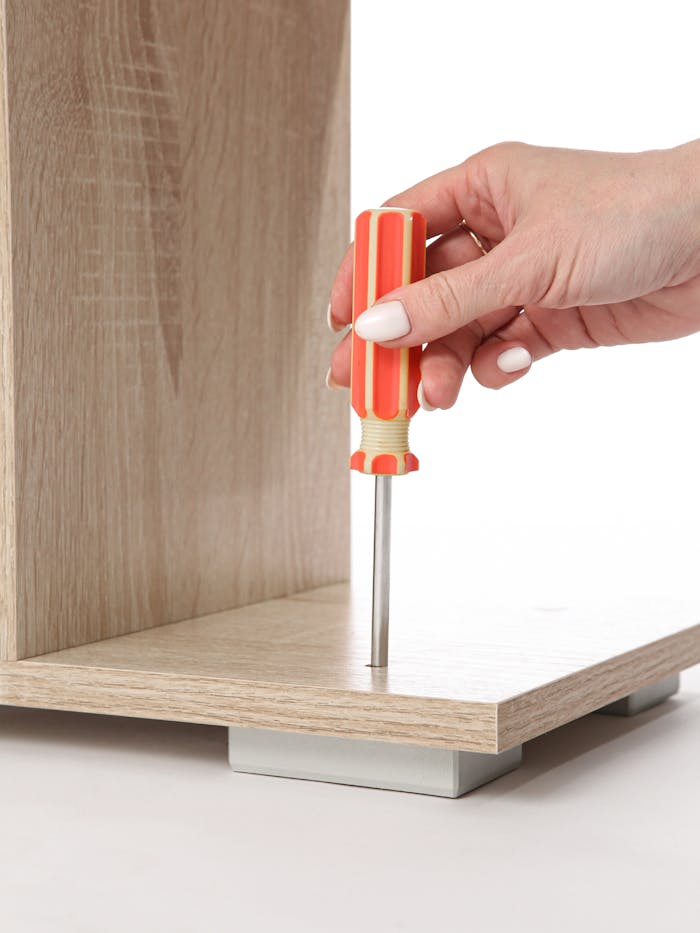 Close-up of a hand using a screwdriver to assemble wooden furniture against a white background.